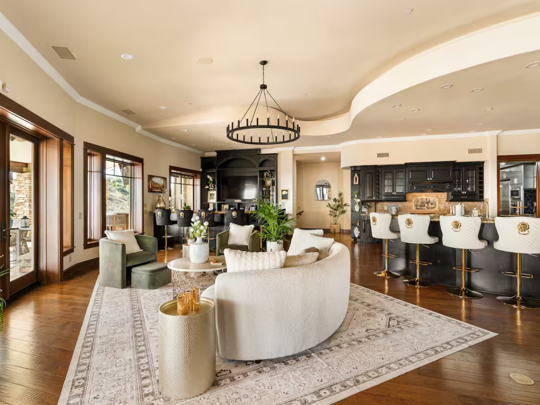 Estate great room with curved sofa, chandelier, and bar overlooking the valley